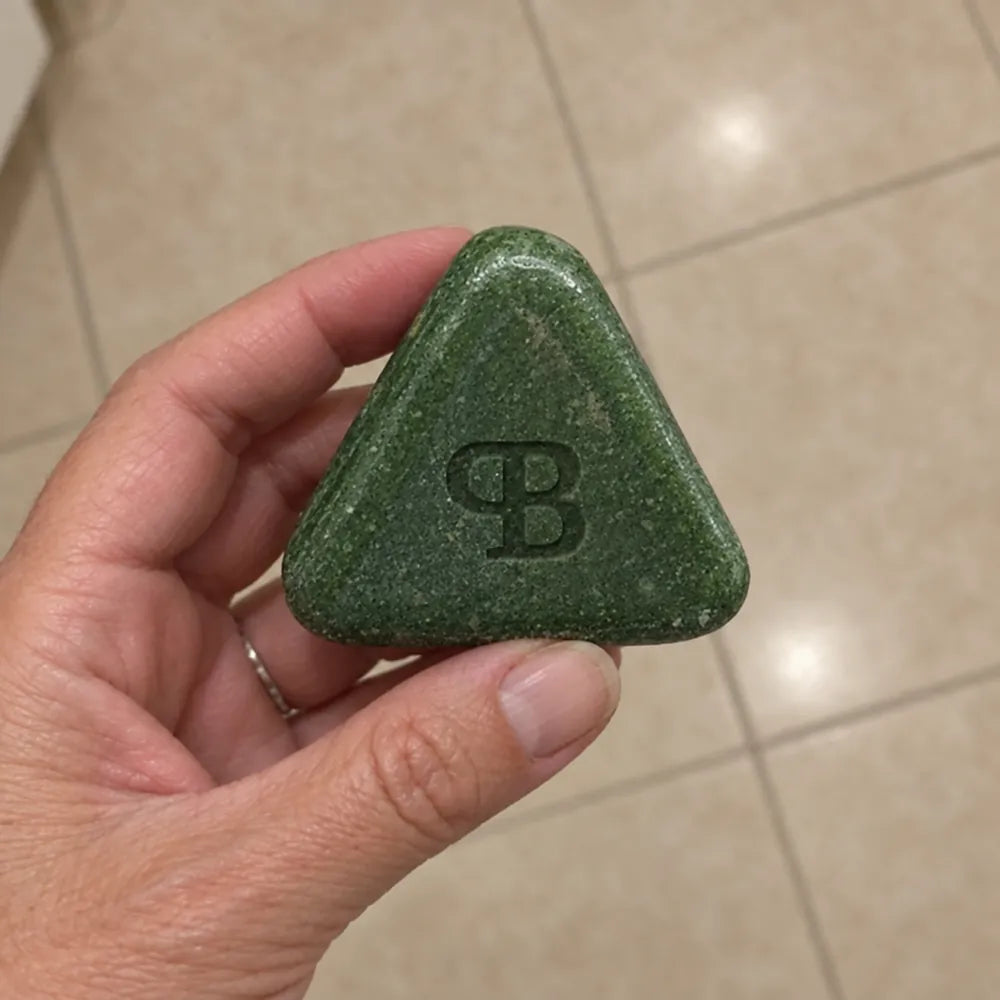 Une main tient la barre Fraîche Heure au-dessus du carrelage de la salle de bain